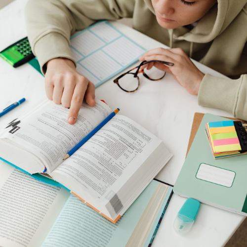 Student studying NEET and JEE exam material with books, notes, and stationery on a study desk.